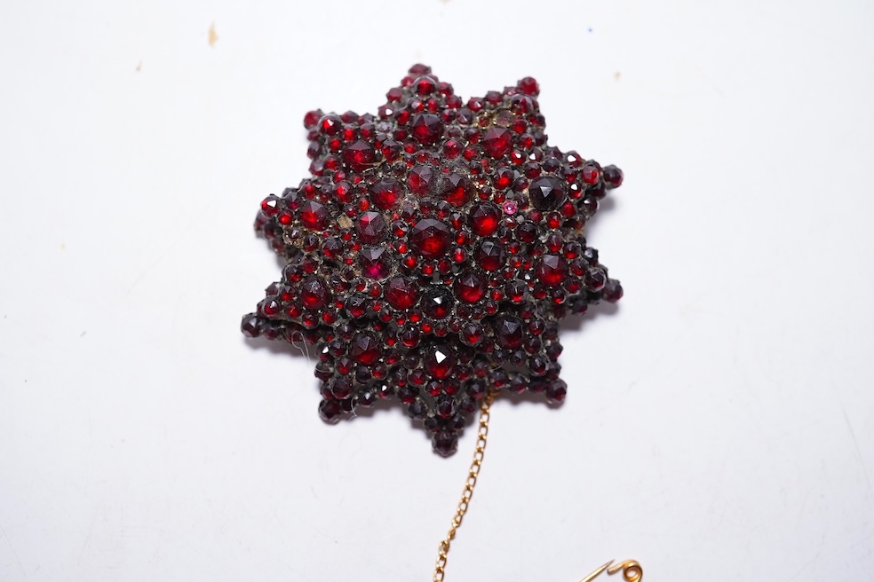 A suite of garnet and paste jewellery, comprising: a brooch, 5cm diameter; a bangle, inner circumference 16cm; two rings, sizes I and M; a pair of earrings, and a single earring, each set with rose-cut garnets; and a pai